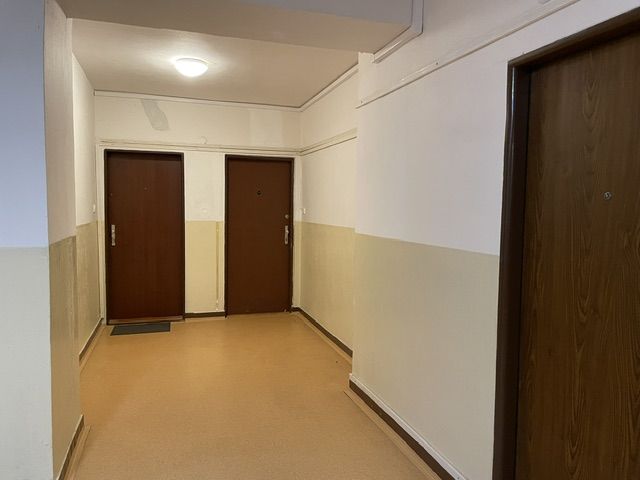 Chodba bytového domu se třemi dveřmi a světlou stěnou.