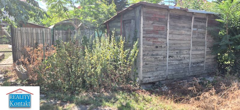 Dřevěný přístřešek obklopený vegetací na dvoře u ulice Za 3 mosty v Nových Zámcích.