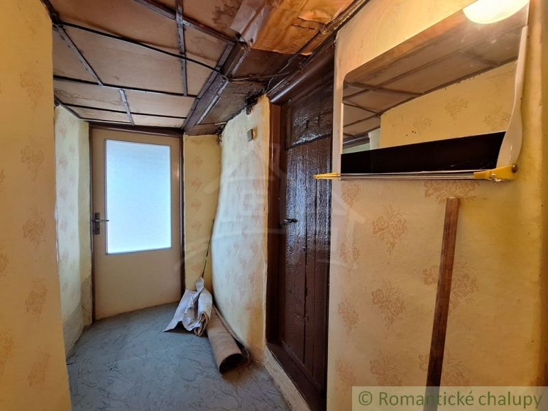 Chodba ve venkovském domě s dřevěným stropem a dekorativní tapetou na stěnách.