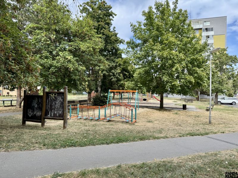Dětské hřiště obklopené stromy v parku města Topoľčany blízko 1-pokojového bytu.