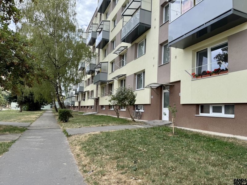 Bytový dům se zelení a chodníkem, nacházející se v Topoľčanech, obklopený stromy.