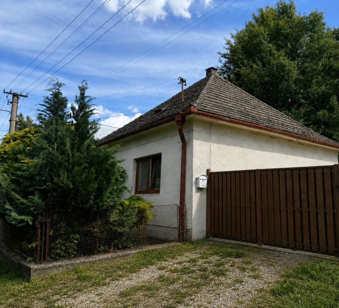 Rodinný dům v Urmincích na ulici Klačany, obklopený dřevinami a plotem.