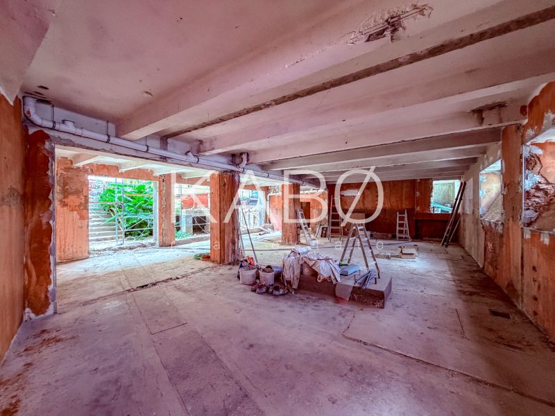 Nedokončené obchodní prostory s betonovou podlahou, žebříky a stavebním materiálem.