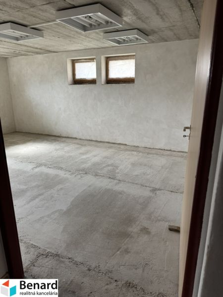 Nevybavená místnost v rodinném domě se dvěma malými okny a surovou podlahou.