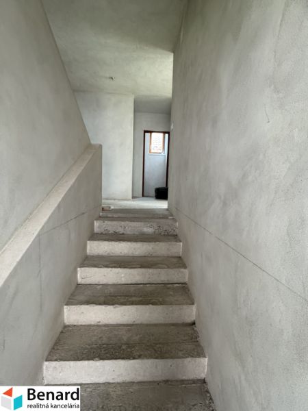 Betonové schody vedoucí do patra v rodinném domě s omítnutými stěnami.