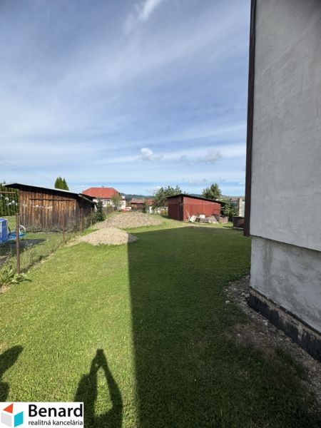 Travnatý dvůr u rodinného domu v Plavnici s výhledem na další zástavbu.