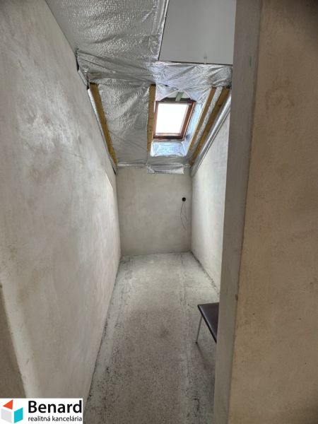 Úzká místnost s betonovou podlahou a střešním oknem v rodinném domě.