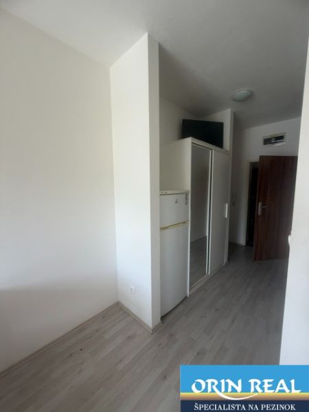 Garsonka s podlahou s dřevěným dekorem, lednicí a vestavěnou skříní.