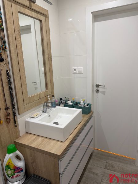 Koupelna v 2-pokojovém bytě s umyvadlem a nábytkem s dřevěným dekorem.