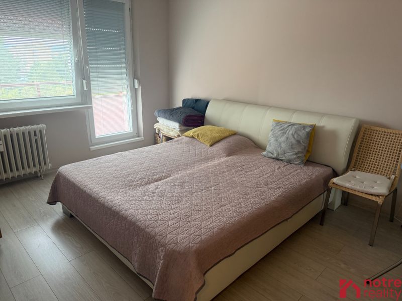 Ložnice s postelí, dřevěným dekorem podlahy a křeslem ve 2-pokojovém bytě.