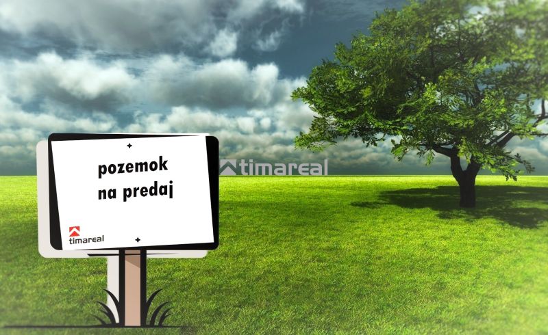 Tabule oznamuje prodej pozemku, zobrazený je zelený trávník vedle stromu.