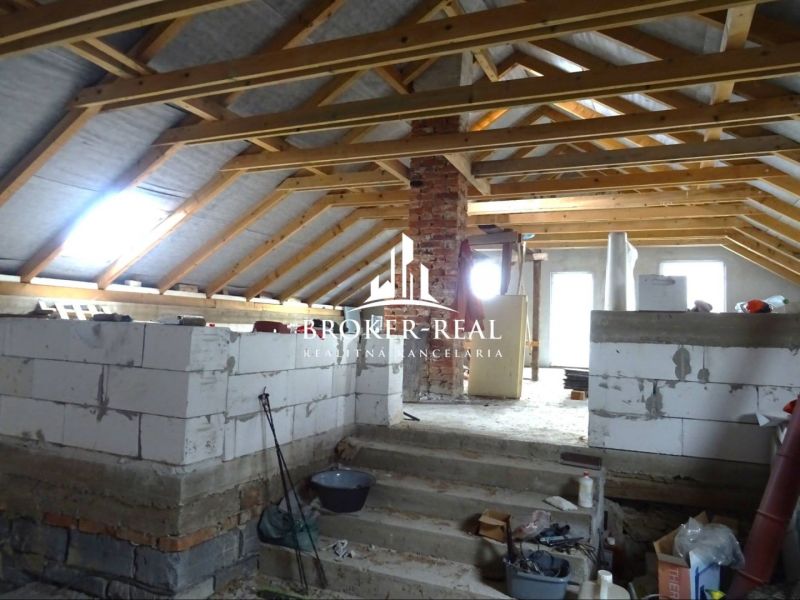 Rozestavěný podkrovní prostor v rodinném domě, s viditelnými dřevěnými trámy a stavebním materiálem.