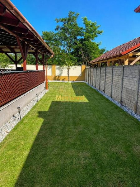 Zahrada rodinného domu v Darnózseli s trávníkem, pergolou a okolím ze stromů.