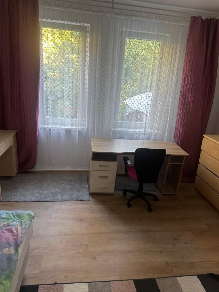 Pokoj s dřevěným dekorem, psací stůl, kancelářská židle a komoda se šuplíky.
