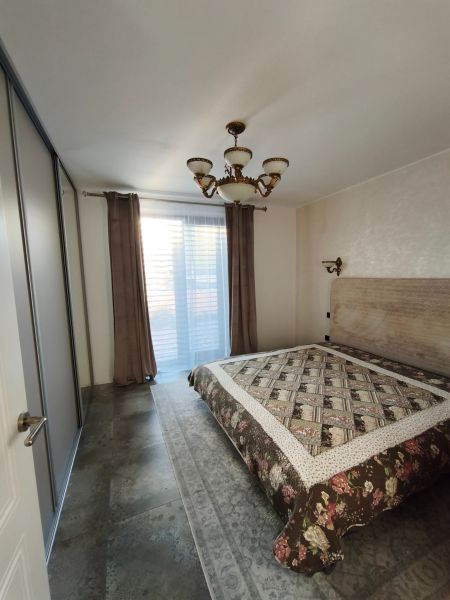 Ložnice v rodinném domě s velkou postelí, skříňkami a elegantním lustrem.