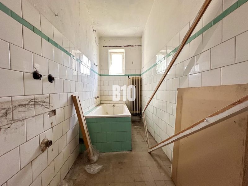 Koupelna rodinného domu s opotřebovanými dlaždicemi a vanou čekající na renovaci.