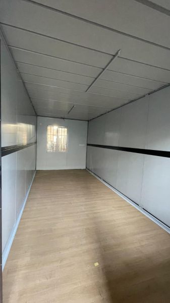 Interiér chaty s podlahou s dřevěným dekorem, bílými stěnami a malým oknem.
