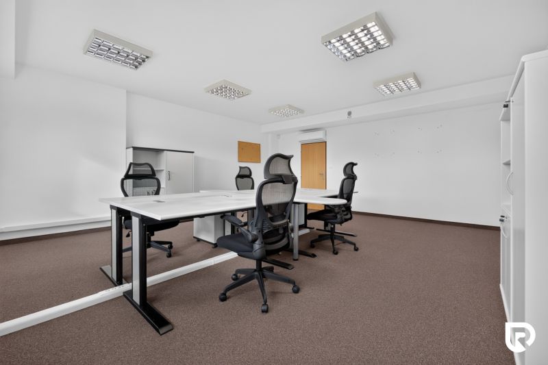 Kanceláře s konferenčním stolem, ergonomickými židlemi a úložnými skříněmi.