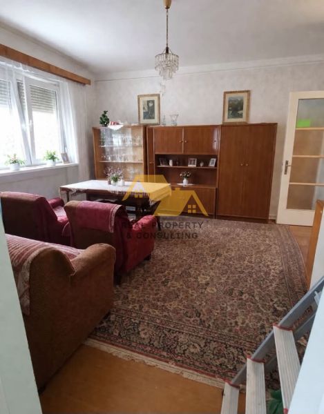 Obývací pokoj v rodinném domě s sedací soupravou, skříňkou a lustrem, podlaha s dřevěným dekorem.