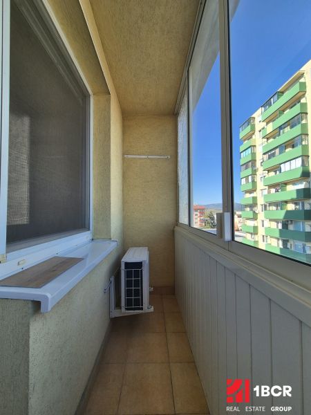 Zasklený balkon v garsonce s klimatizací a výhledem na bytovky.