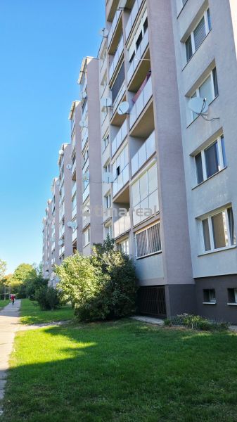 Exteriér panelového domu v Trnavě se zelení a chodníkem k 3-pokojovému bytu.
