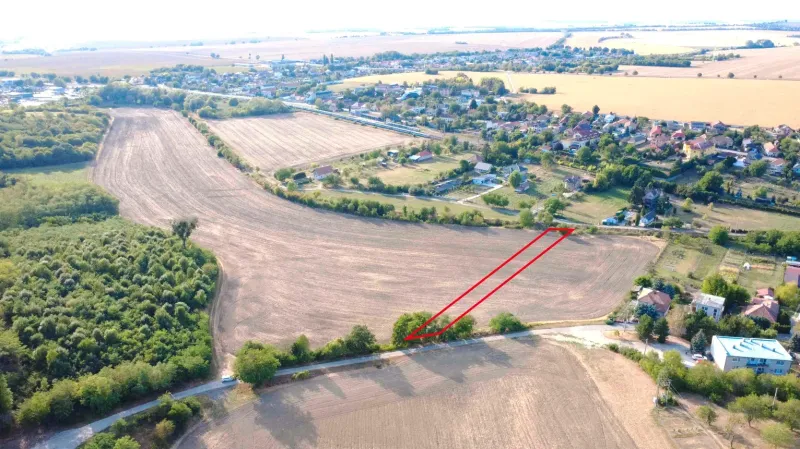 Zemědělské a lesní pozemky v Podhájské, okolní pole a vzdálené budovy.