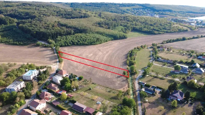 Záběr na zemědělské a lesní pozemky v Podhájské, obklopené domy a silnicemi.