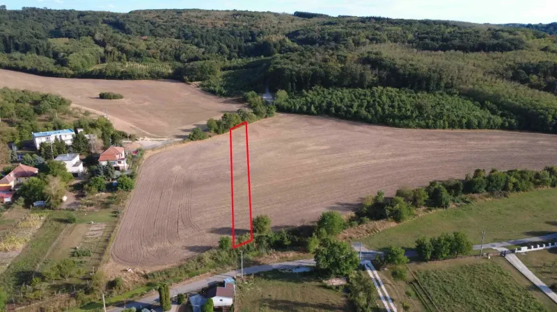 Venkovský výhled na zemědělské a lesní pozemky v Podhájské obklopující osídlení s rodinnými domy.