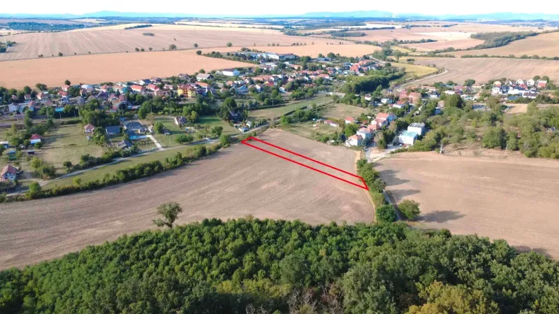 Letecký pohled na zemědělské a lesní pozemky v Podhájské, s vesnicí v pozadí.