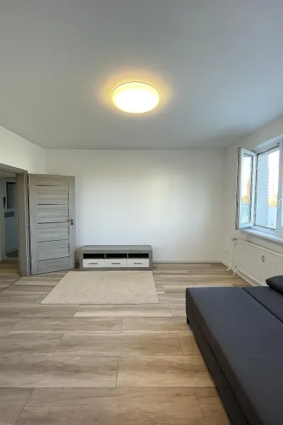 Světlý obývací pokoj v 2-pokojovém bytě s podlahou s dřevěným dekorem a šedou pohovkou.