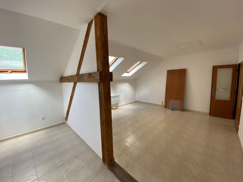 Podkrovní kancelář s dřevěnými trámy a šikmými okny, podlaha s dřevěným dekorem.