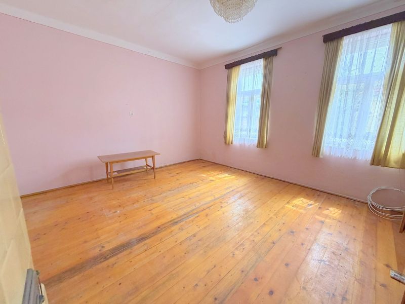 Pokoj rodinného domu s podlahou s dřevěným dekorem, stolkem a záclonami.