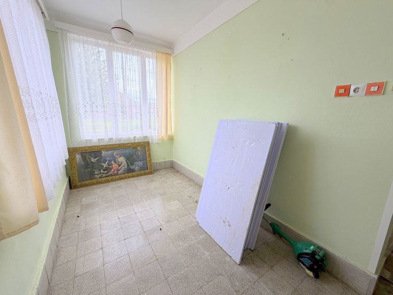 Interiér rodinného domu s obrazem, okny s bílými záclonami a zelenými stěnami.