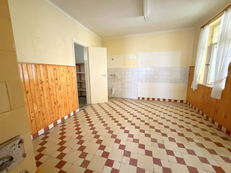 Kuchyně v rodinném domě s dlažbou a dřevěným obkladem na stěnách.