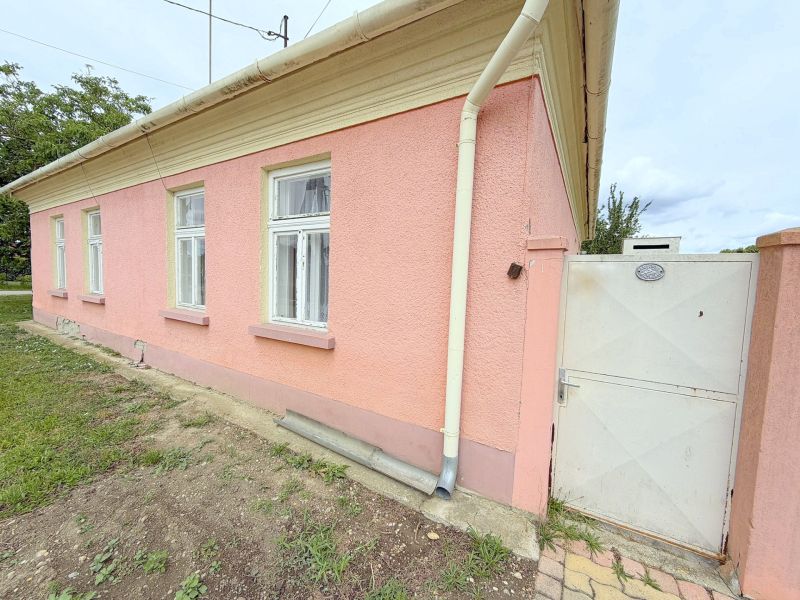 Rodinný dům v Dunakiliti s růžovou fasádou, bílými okny a brankou.