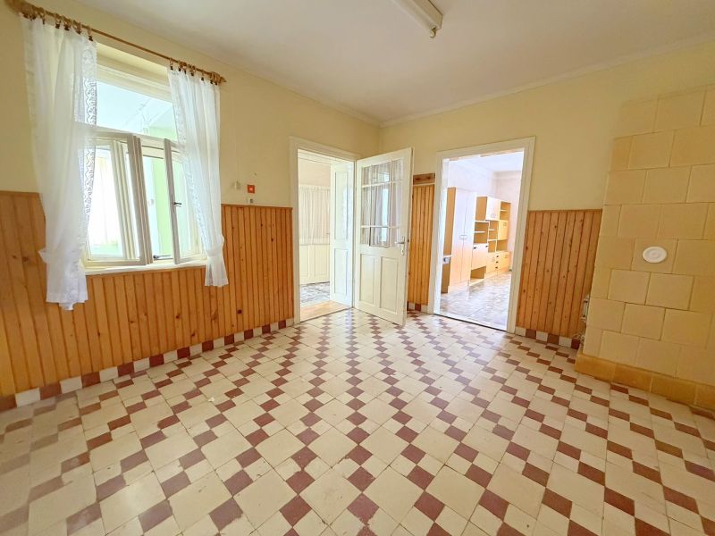 Interiér rodinného domu, světlá místnost s dlaždicovou podlahou a dřevěným obložením stěn.