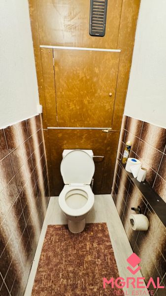Toaleta v 3-pokojovém bytě s hnědými obklady a rohožkou.