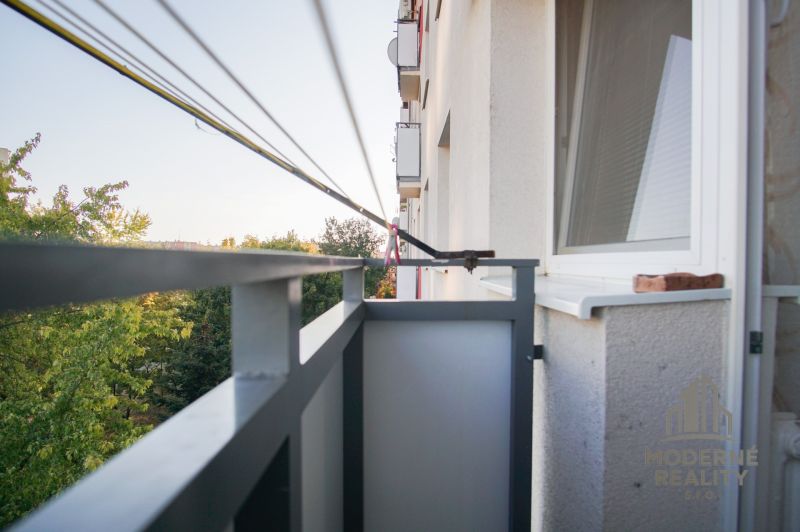 Balkon 2-pokojového bytu v Nových Zámcích s výhledem na zelené stromy.