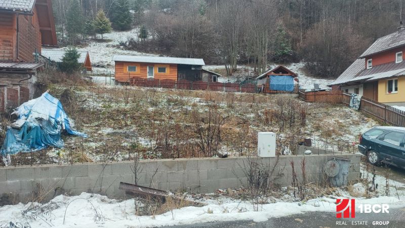 Sněhem pokrytý pozemek s rodinným domem v Oščadnici obklopený zelení a dřevěnými strukturami.