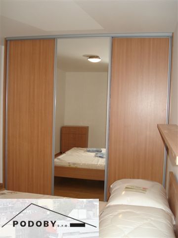 Ložnice ve 3pokojovém bytě s velkou vestavěnou skříní a podlahou s dřevěným dekorem.