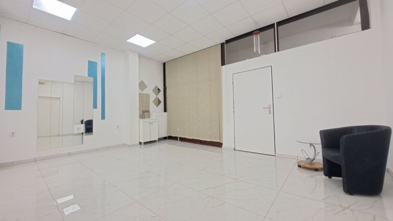 Interiér obchodních prostor s křeslem, zrcadly a dlažbou s bílým vzorem.