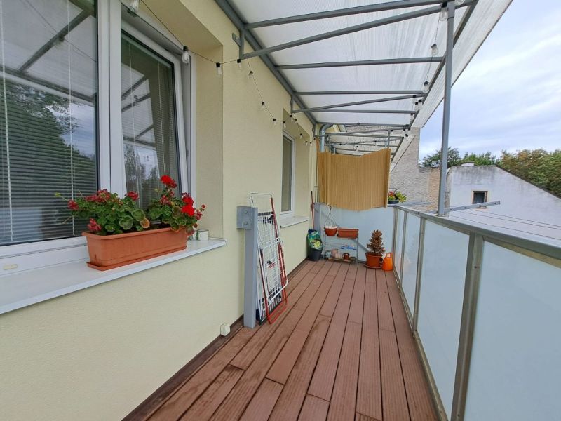 Balkon 3pokojového bytu s podlahou s dřevěným dekorem, květináčem a sušákem na prádlo.
