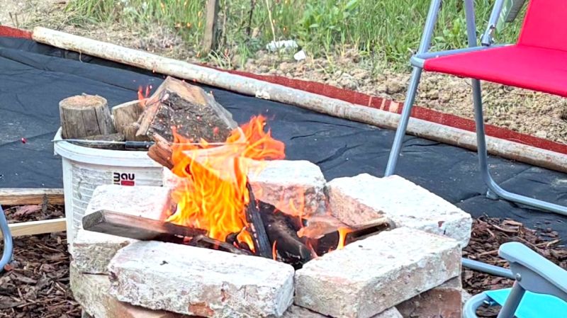 Ohniště obklopené cihlami a židlemi na zahradě rodinného domu.