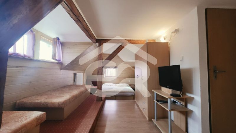 Interiér rekreačního apartmánu s postelí, televizorem a podlahou s dřevěným dekorem.