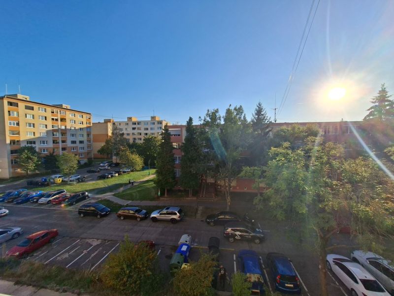 Auta parkují na ulici Benedikta v Prievidzi u garsonky, slunečný den.