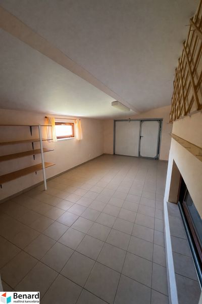 Interiér rodinného domu s dlažbou, úložnými policemi a oknem s jemnými závěsy.