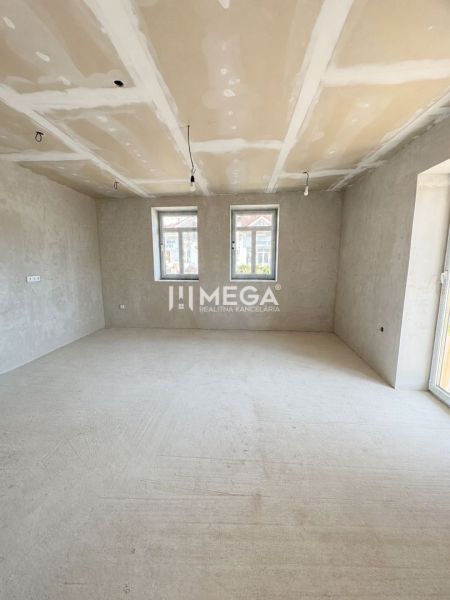 Prostorný pokoj v rodinném domě s velkými okny a betonovou podlahou.