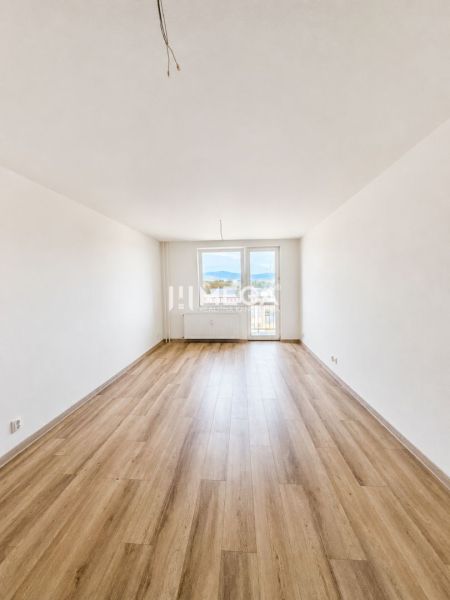 Prostorný obývací pokoj se vstupem na balkon a podlahou s dřevěným dekorem v 2pokojovém bytě.