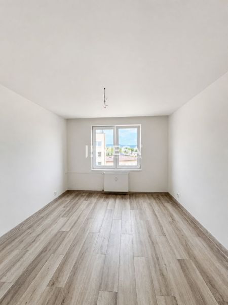Světlý prázdný prostor s bílými stěnami a podlahou s dřevěným dekorem v 2-pokojovém bytě.