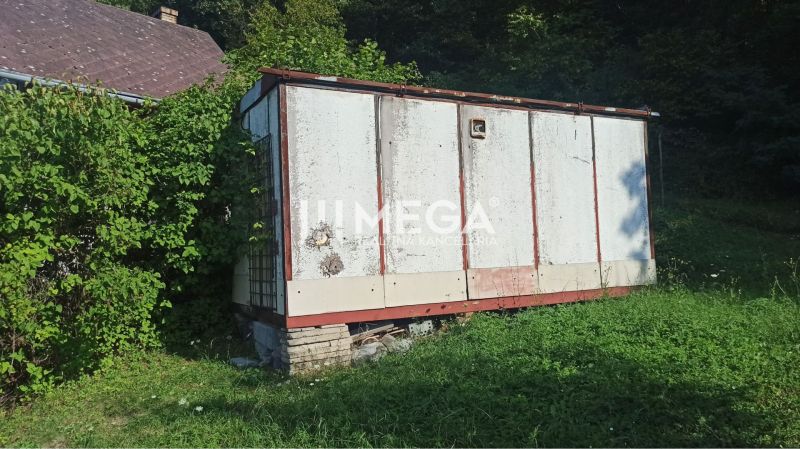 Starší sklad na zahradě ulice v Humenném, obklopený zelení a rostoucí trávou.